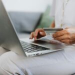Close-up of a person holding a credit card while shopping online using a laptop at home.